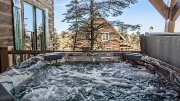 A hot tub with a view of a wooden building and a pine tree.