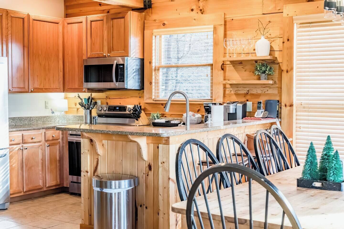 A wooden cabin-style kitchen with a central island, stainless steel appliances, and a dining area with chairs.