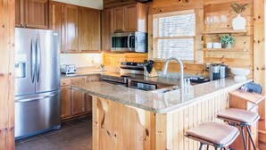Een moderne keuken met houten kastjes, roestvrijstalen apparatuur, een granieten aanrecht en een bar met barkrukken.