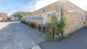A brick building with a gated entrance, a paved sidewalk, and a small garden area with a palm tree. - Vibrant 1BD Flat - 8 Mins to Dalston, Hackney! (London)