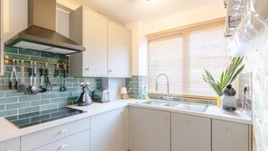 A modern kitchen with a built-in stove, a large window with blinds, and a variety of kitchen utensils on the wall. - Vibrant 1BD Flat - 8 Mins to Dalston, Hackney! (London)
