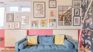 A room with a blue sofa, framed artwork on the walls, and a radiator. - Vibrant 1BD Flat - 8 Mins to Dalston, Hackney! (London)