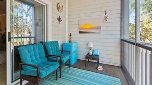 A porch with wicker chairs, a small table, a lamp, and a painting of a sunset. - Willow Bend, Beautiful 2nd floor Villa  2Bedroom/2Bath, WiFi (North Myrtle Beach)
