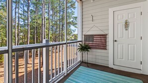 A porch with a view of tall trees, a white door with a small sign, and a hanging American flag. - Willow Bend, Beautiful 2nd floor Villa  2Bedroom/2Bath, WiFi (North Myrtle Beach)