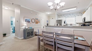A dining area with a wooden table and chairs, a chandelier, and a kitchen in the background. - Willow Bend, Beautiful 2nd floor Villa  2Bedroom/2Bath, WiFi (North Myrtle Beach)