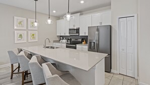 Une cuisine moderne avec des armoires blanches, des appareils en acier inoxydable et des luminaires suspendus.