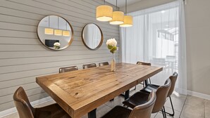 Un coin repas comprenant une table en bois, six chaises, trois lampes suspendues et deux miroirs ronds accrochés au mur.