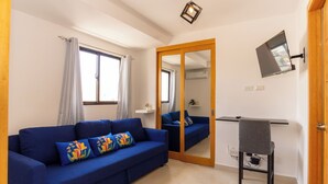 Una stanza con un divano blu, un tavolino, uno specchio, una televisione e una porta.