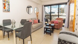 Un soggiorno moderno con un tavolo da pranzo in vetro, divani grigi e una grande finestra con vista sulla città.