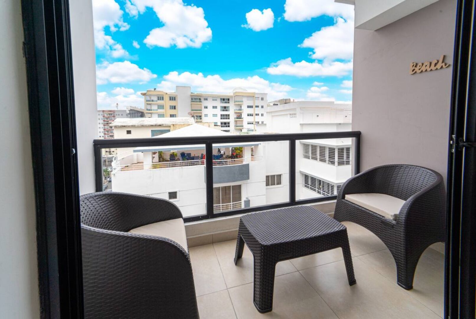 Un balcone con mobili in vimini, vista su edifici e un cartello con la scritta 'Beach'.