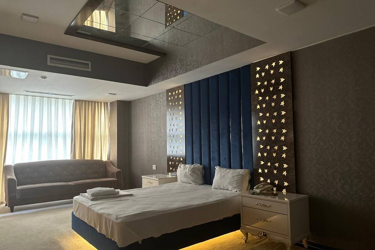 Quarto de hotel moderno com uma cama grande, um sofá, uma mesinha de cabeceira e uma parede com painel decorativo.