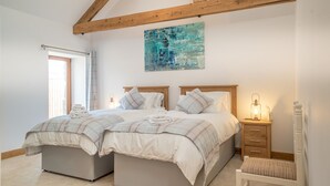 Une chambre avec deux lits, un plafond en bois, un tableau, une table de chevet et une chaise.