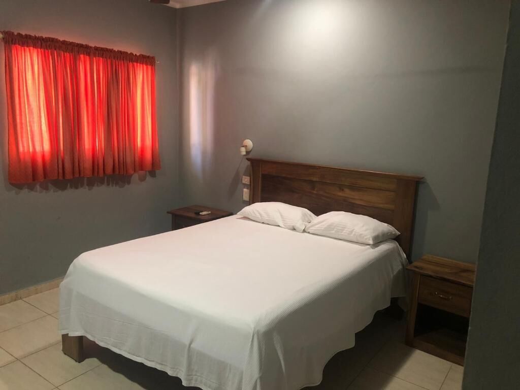 Ein Schlafzimmer mit einem hölzernen Bettgestell, weißer Bettwäsche, einem Nachttisch und einem roten Vorhang.