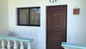 A room with a wooden door, a window with a curtain, and a small potted plant on the wall. - Hotel Cambri (Nagua)