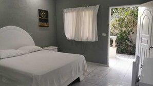 A bedroom with a bed, a nightstand, a window with curtains, and a door leading to an outdoor area. - Hotel Cambri (Nagua)