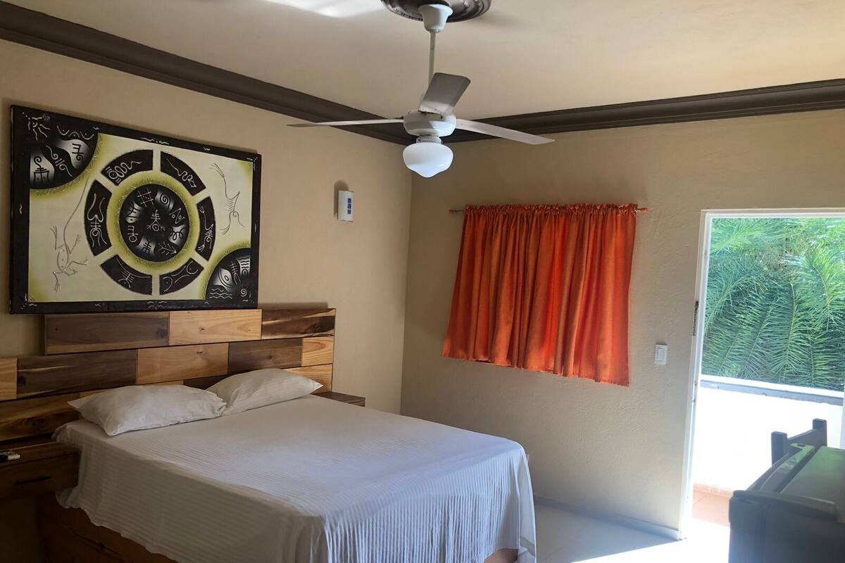 A bedroom with a bed, a ceiling fan, a window with curtains, and a wall-mounted air conditioning unit.