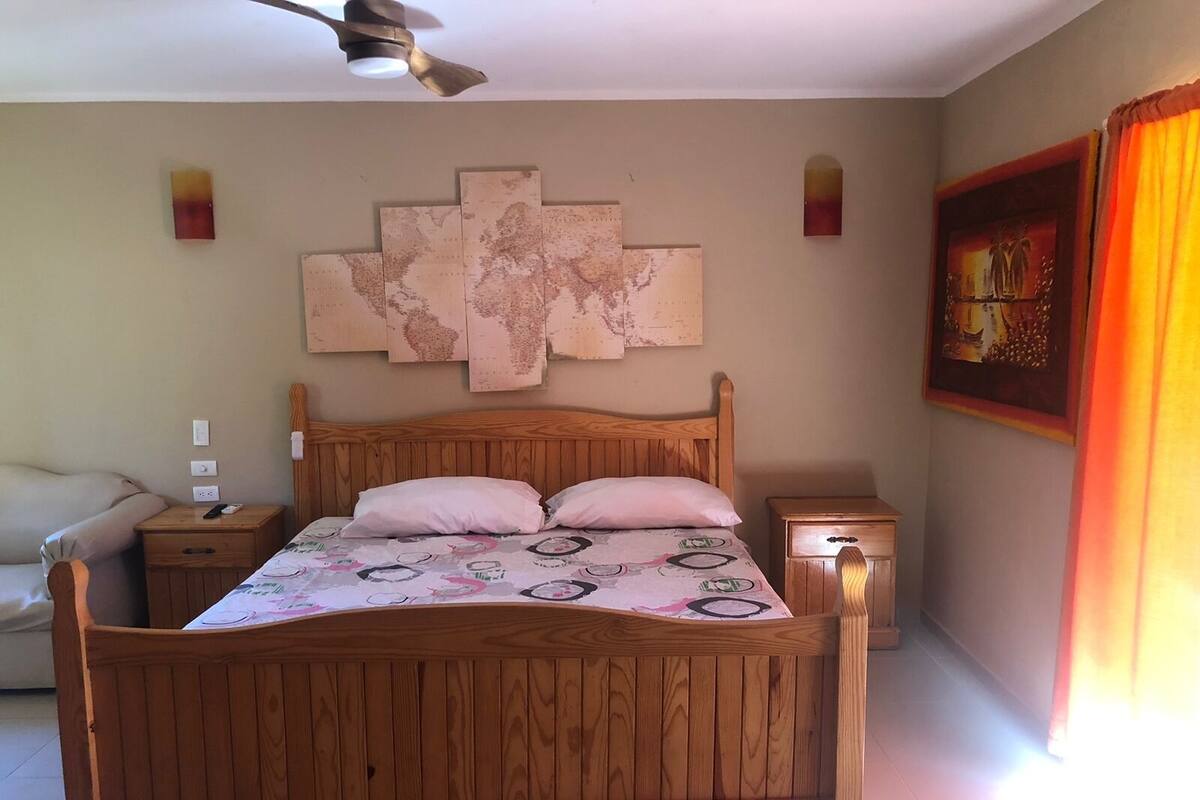 A wooden bed with a headboard, two bedside tables, a ceiling fan, and a world map artwork on the wall.