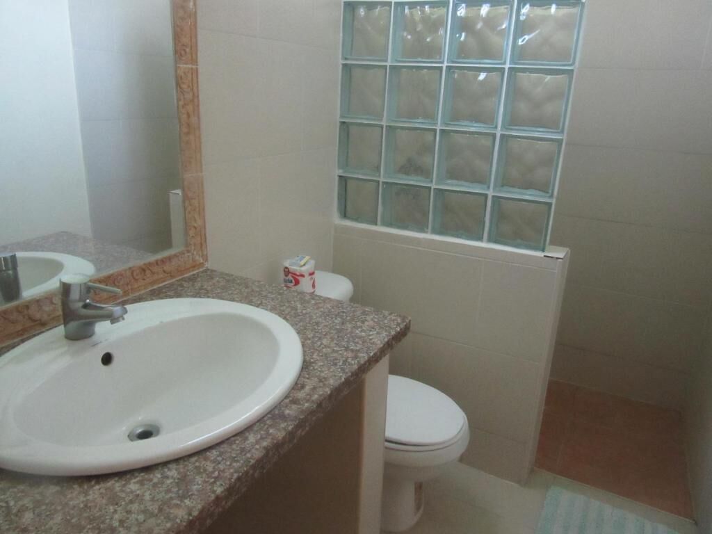 Een badkamer met een wastafel met een granieten blad, een spiegel, een toilet en een raam met geëtst glas.