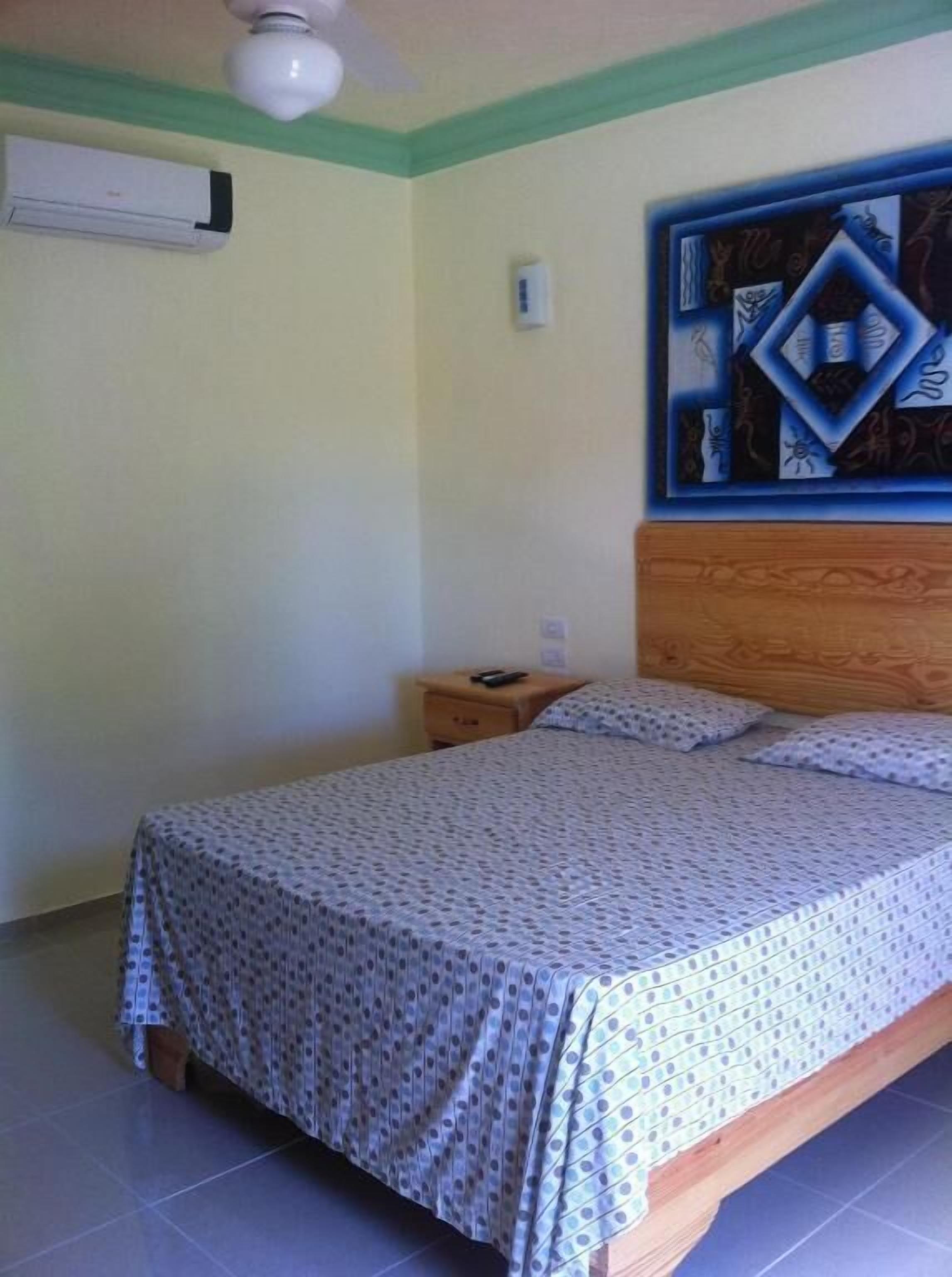 A bedroom with a bed, a nightstand, a ceiling fan, and a wall-mounted air conditioner.