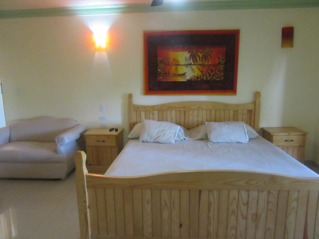 Una cama de madera con ropa de cama blanca, una mesita de noche, una lámpara y un cuadro en la pared.