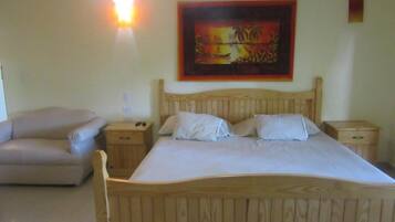Una cama de madera con ropa de cama blanca, una mesita de noche, una lámpara y un cuadro en la pared.