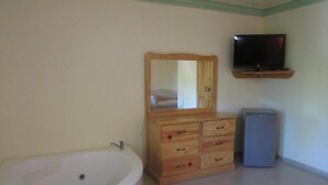 A bathroom with a bathtub, wooden vanity, a mirror, a television, and a small refrigerator. - Hotel Cambri (Nagua)