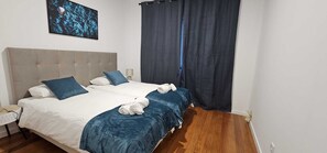 A double bed with a grey headboard, two blue pillows, and a white blanket.