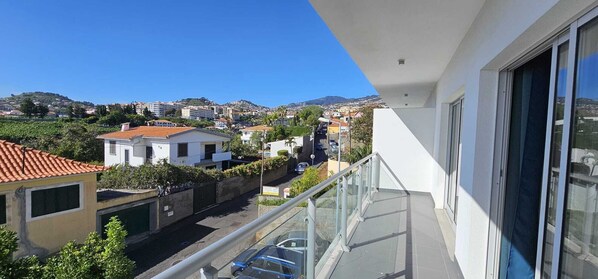 Un balcón con vista despejada a una calle residencial y colinas lejanas.