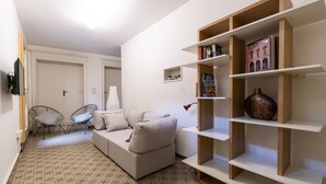 Ein Wohnzimmer mit einer Couch, zwei Sesseln, einem Bücherregal und einem an der Wand montierten Fernseher.