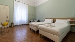 Ein Zimmer mit zwei Betten, einem Sessel, einem kleinen Tisch und einem Fenster mit Vorhängen.