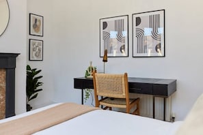 A bedroom with a bed, a desk, and a chair. There are three framed artworks on the wall.
