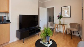 Una sala de estar moderna con televisor de pantalla plana, una mesa de comedor con sillas y una zona de cocina con armarios y electrodomésticos.