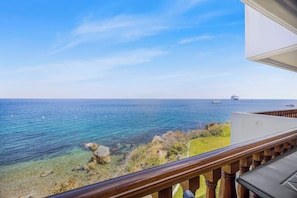 A balcony with a view of the sea, a ship in the distance, and a rocky shoreline.