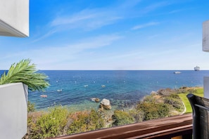 A balcony with a view of the sea, boats, and a distant ship.