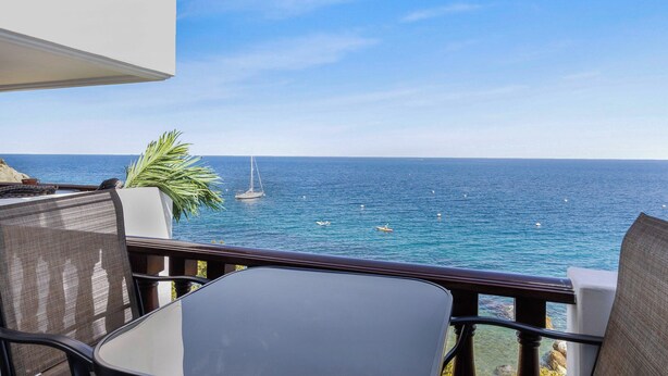 Een balkon met uitzicht op zee, een zeilboot en een palmboom.