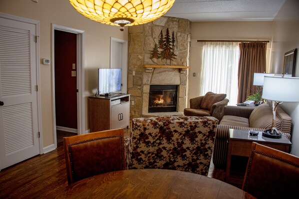 A living room with a stone fireplace, a television, a sofa, and a dining area with a table and chairs.