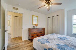 Un dormitorio con piso de madera, una cama con cubrecama floral, un aparador, un ventilador de techo y dos armarios.