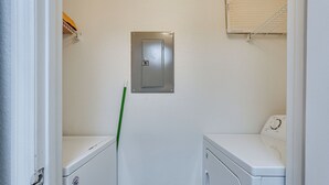 Een wasserette met twee witte wasmachines, een metalen opslagkist, en een groene bezem die tegen de muur staat.