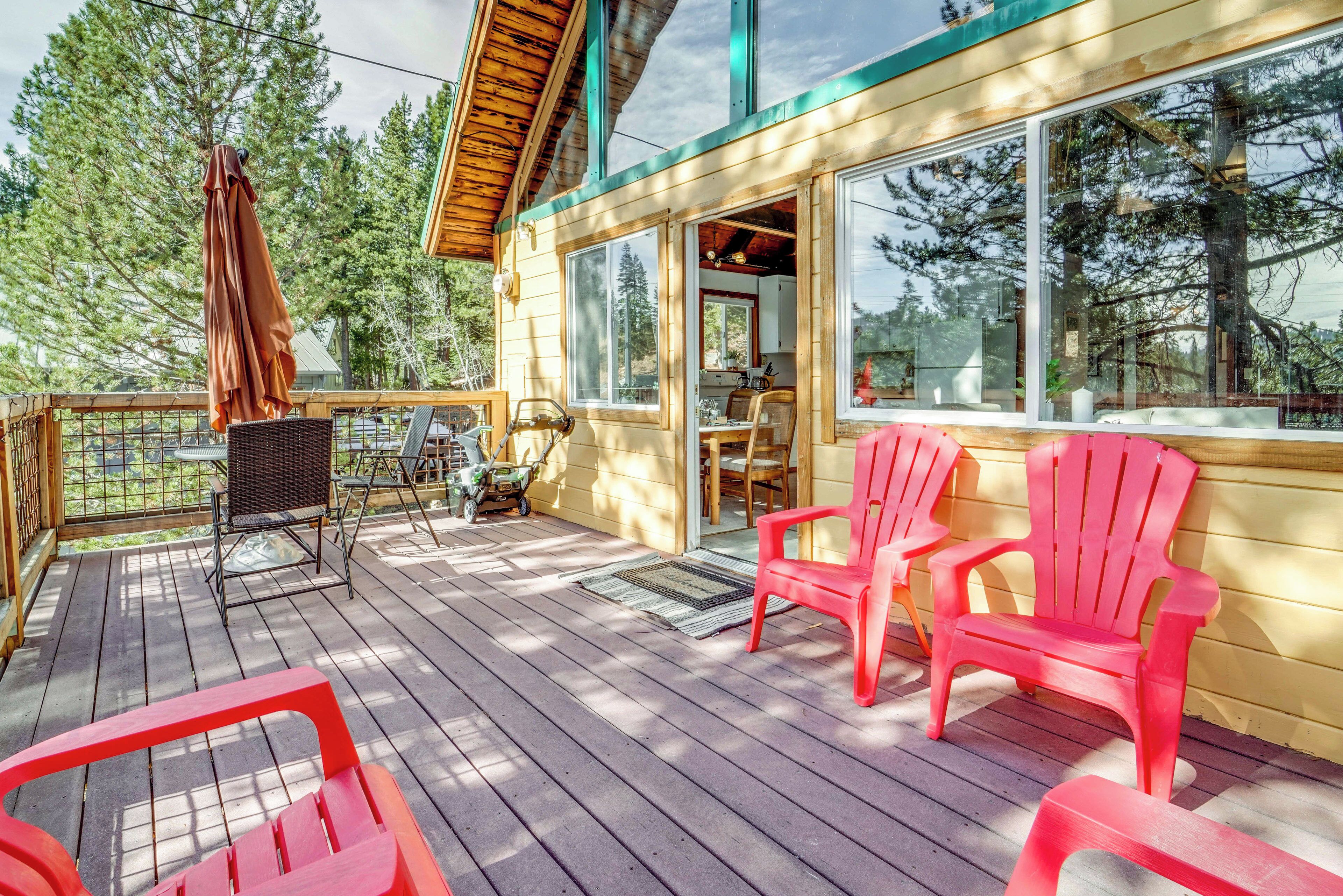 A wooden deck with red chairs, a wicker chair, and a small table.