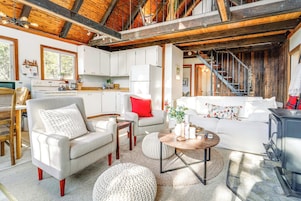 Una sala de estar acogedora con chimenea, comedor y cocina con armarios blancos.