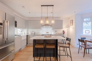 A modern kitchen with a central island, pendant lights, and stainless steel appliances. - Newly Refurbished 2BD Flat - Wimbledon Village! (London)