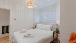 A bedroom with a large bed, white bedding, a green lamp, and a window with blinds. - Newly Refurbished 2BD Flat - Wimbledon Village! (London)