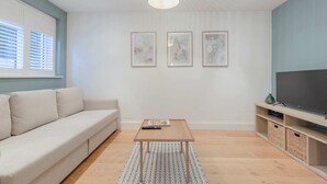 A modern living room with a sofa, a coffee table, a TV on a stand, and three framed artworks on the wall. - Newly Refurbished 2BD Flat - Wimbledon Village! (London)