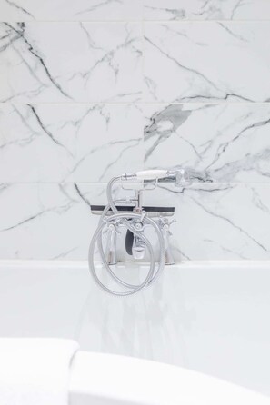 A bathroom with a marble backsplash and a chrome showerhead with a handheld shower attachment. - Newly Refurbished 2BD Flat - Wimbledon Village! (London)