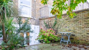A courtyard with a brick wall, a metal table, and various plants. - Newly Refurbished 2BD Flat - Wimbledon Village! (London)