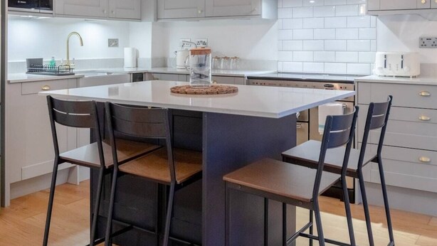 A modern kitchen with a central island, pendant lights, and stainless steel appliances. - Newly Refurbished 2BD Flat - Wimbledon Village! (London)