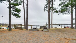 A gravel area with a wooden bench, a metal grill, and a wooden swing set near a lake. - Lakefront Bemidji Getaway w/ Community Beach! (Bemidji)