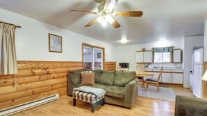 A cozy living room with a wooden floor, a green sofa, a wooden ceiling fan, and a kitchen area in the background. - Lakefront Bemidji Getaway w/ Community Beach! (Bemidji)