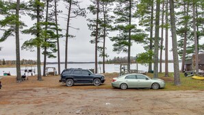 A campground with two cars parked on a dirt area, surrounded by tall pine trees and a body of water in the background. - Lakefront Bemidji Getaway w/ Community Beach! (Bemidji)