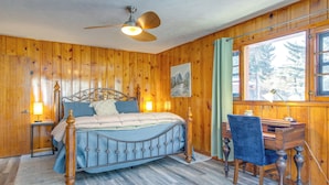 Une chambre aux murs lambrés, comprenant un lit, un bureau, une chaise et un ventilateur de plafond.